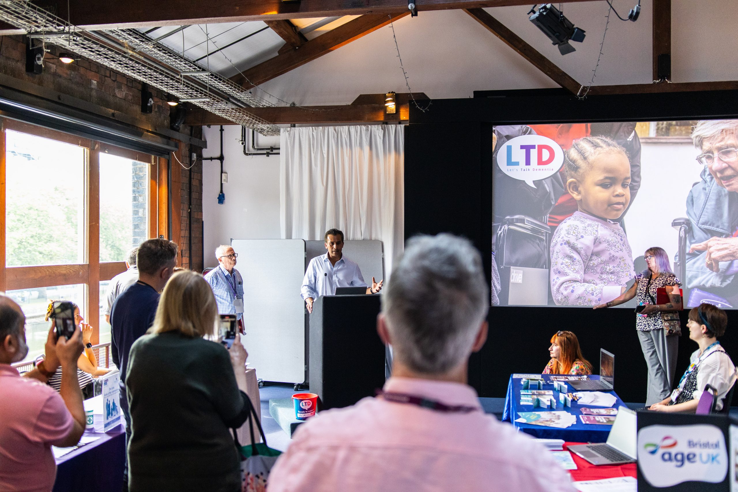 Seb Choudhury (ITV) speaking to a room full of people at Let's Talk Dementia 2024.