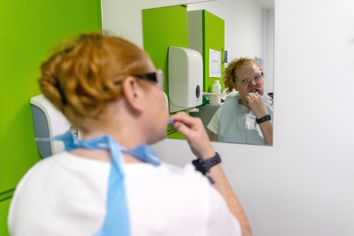 A patient is cleaning her teeth and looking in the mirror.