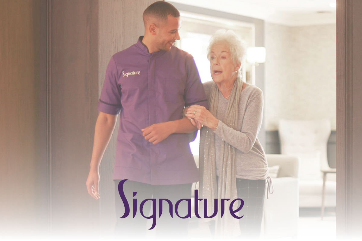 An elderly woman walks arm-in-arm with a smiling caregiver in a purple 'Signature' uniform, inside a well-lit, elegant care home. The 'Signature' logo is displayed at the bottom.