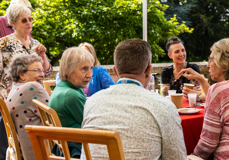 A group of people have a conversation sat around a table with lunch.