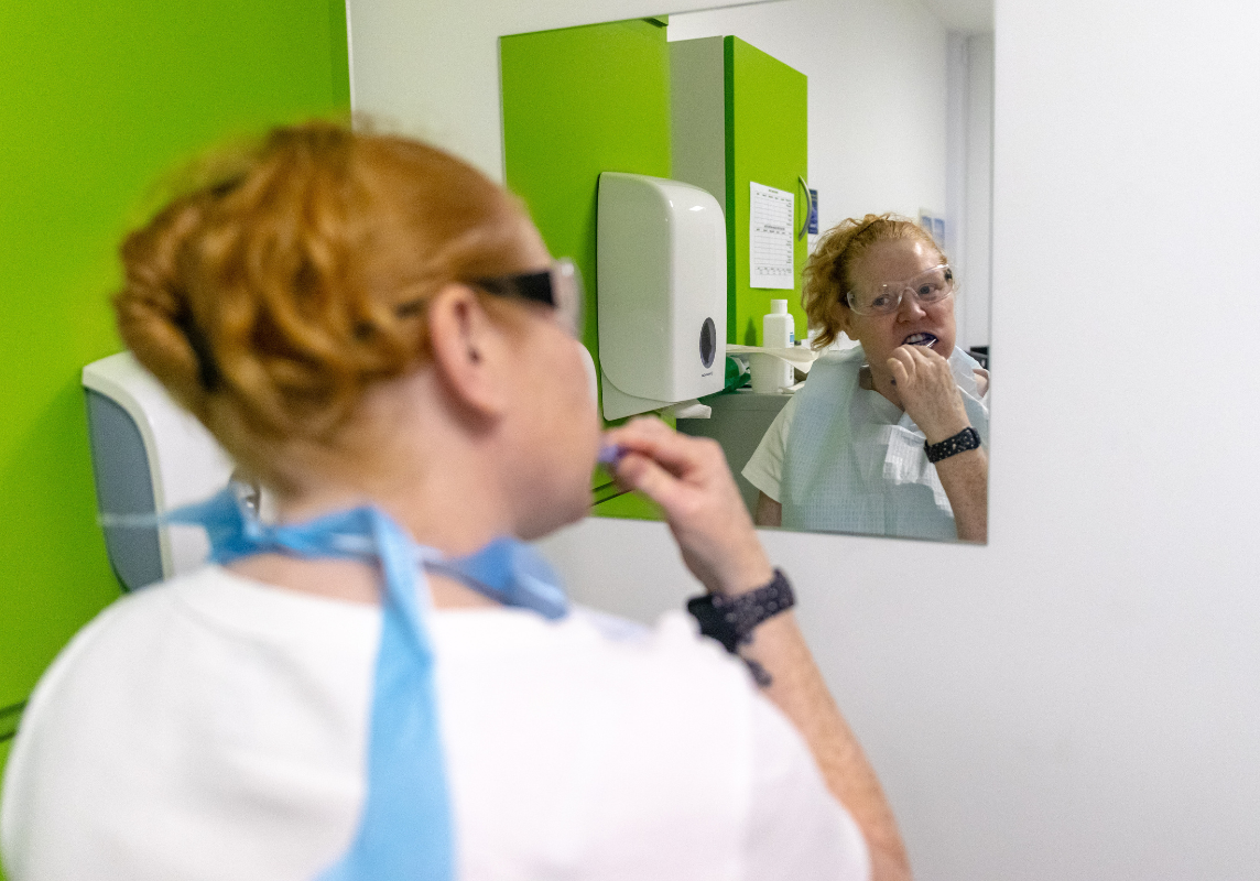 A patient is cleaning her teeth and looking in the mirror.